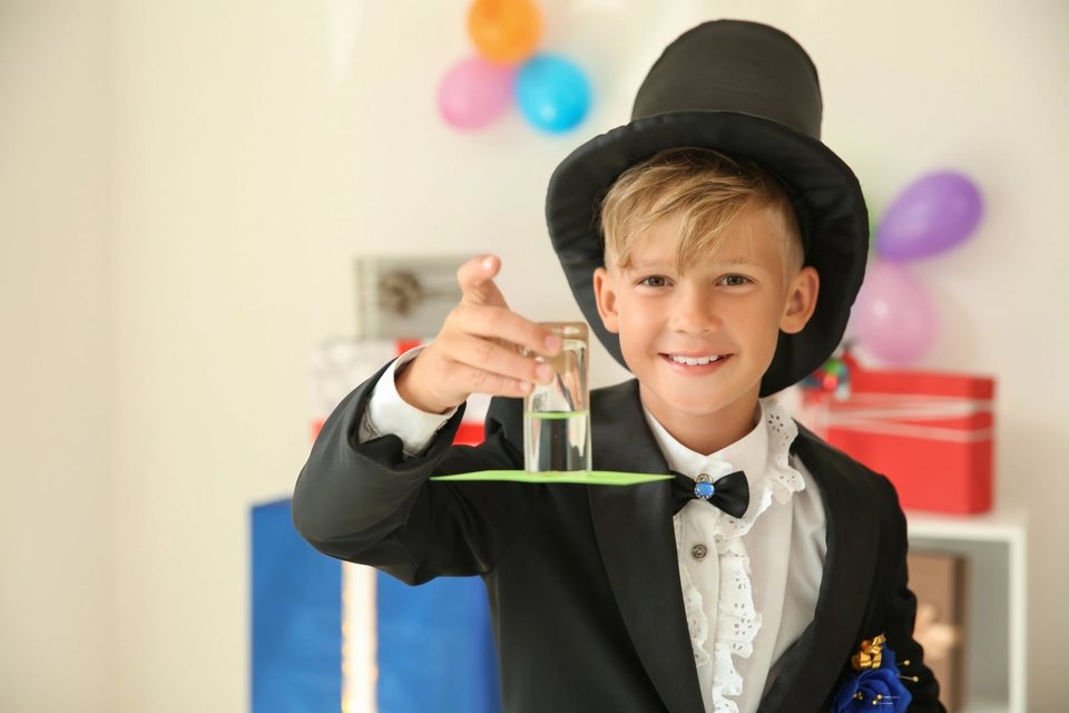 A smiling child magician performing a trick with a glass