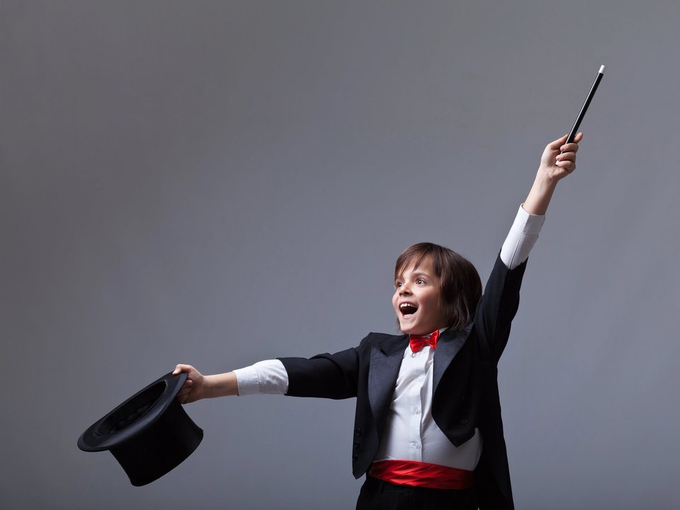 A delighted child magician performing with a wand and top hat